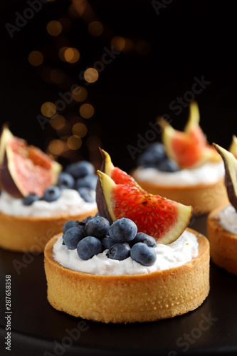 Fototapeta Naklejka Na Ścianę i Meble -  Tarts with blueberries and figs on black table against dark background, closeup. Delicious pastries