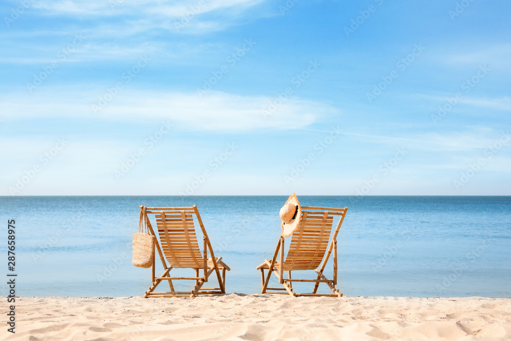 Wooden deck chairs on sandy beach near sea