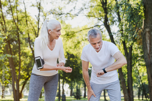 Senior tired man and woman checking pulse after workout outdoors
