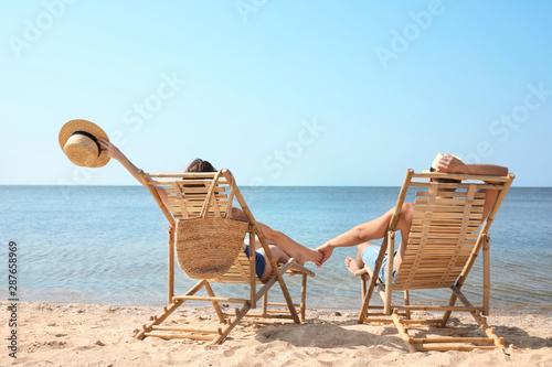 Leinwand Poster Young couple relaxing in deck chairs on beach