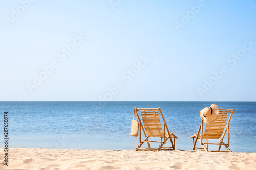 Foto Wooden deck chairs on sandy beach near sea