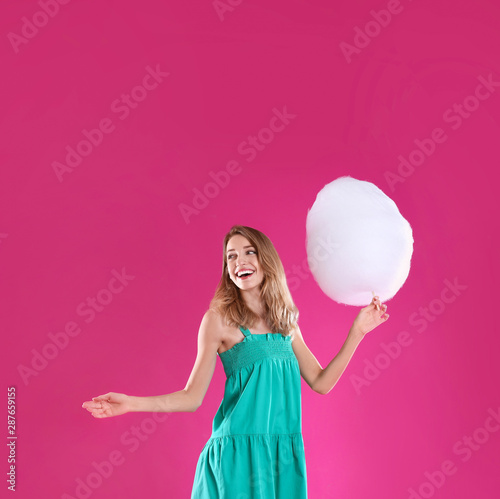 Happy young woman with cotton candy on pink background