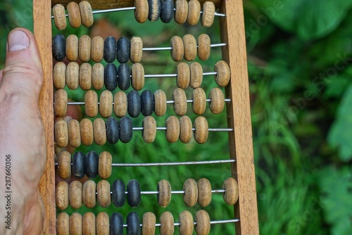 hand holds old brown wooden abacus on a green background