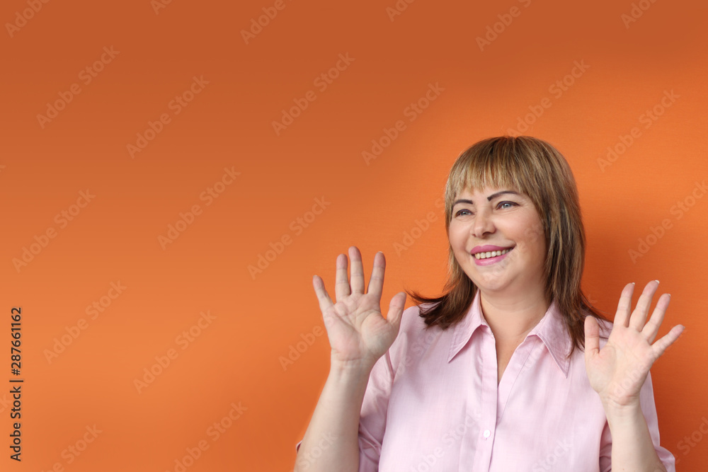 middle-aged European woman is standing, protestingly extending both hands, on an orange background, middle-aged European woman is standing, protestingly extending both hands, on an orange background,
