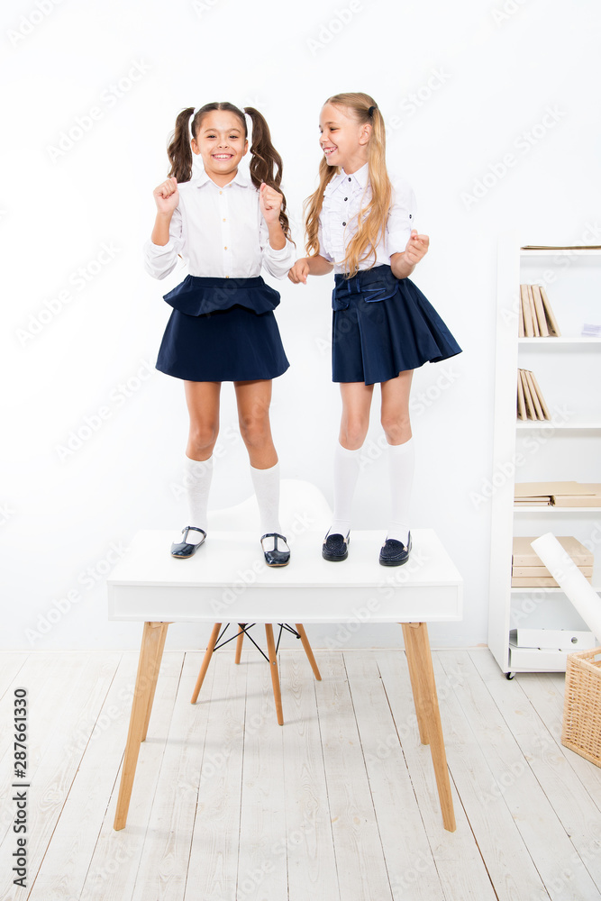 Back to school style. Happy small girls with long hair styles standing on desk in class. Little children smiling in school style. Giving school fashion a sense of style