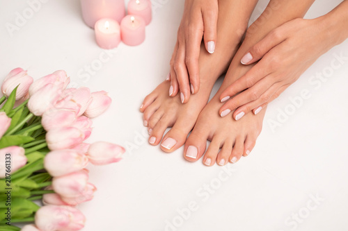 The picture of female legs and hands after pedicure and manicure. Legs are surrounded by pink tulips and candles. © forma82