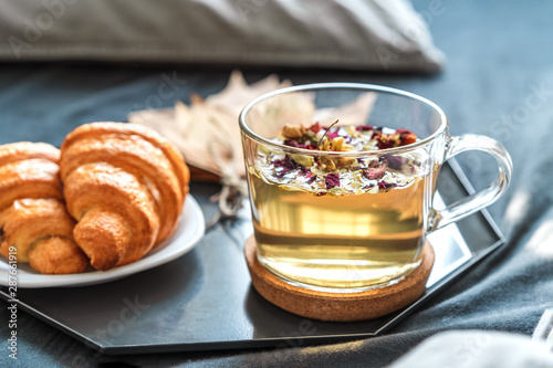 Cozy autumn morning concept. Breakfast with herbal tea and croissants on the bed with grey sheets in a sunny room