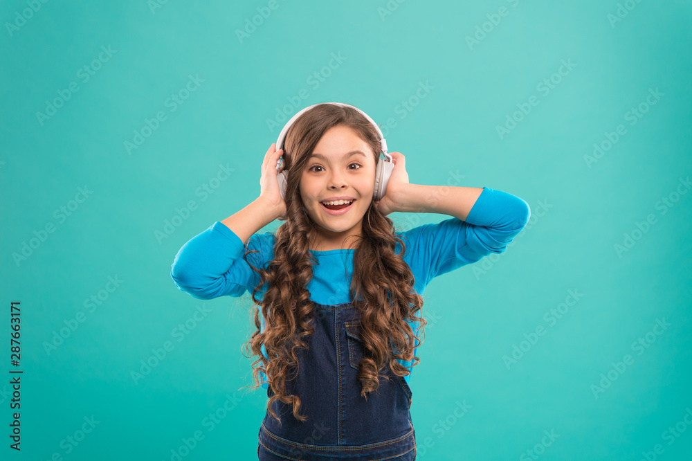 Fototapeta premium Feeling the beauty of the song. Cute small child listening to song on blue background. Adorable little girl enjoying song playing in headphones. Composing a song