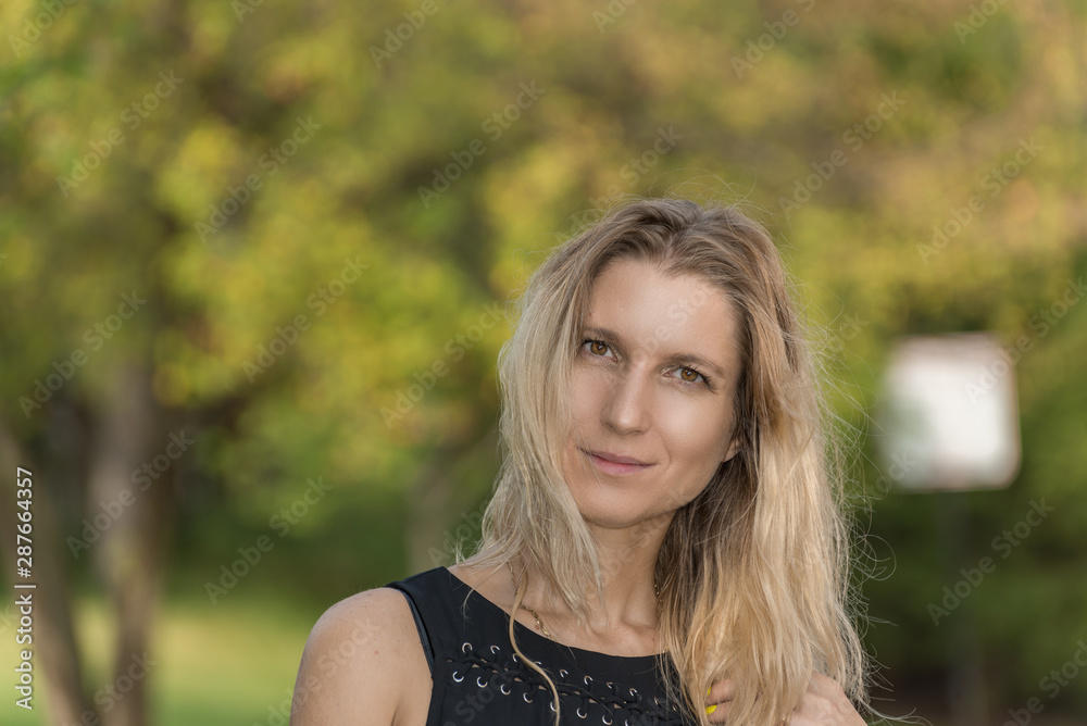 Attractive blonde young woman in a park with blurred background Attractive blonde young woman in a park with blurred background