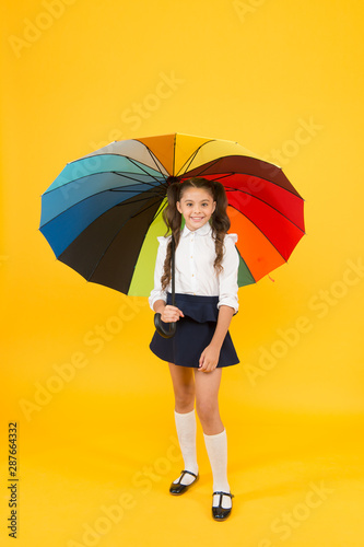 Autumn comes with weather changes. Small child holding colorful umbrella for autumn rain on yellow background. Little kid going to school on autumn day or september 1. Getting ready for autumn term