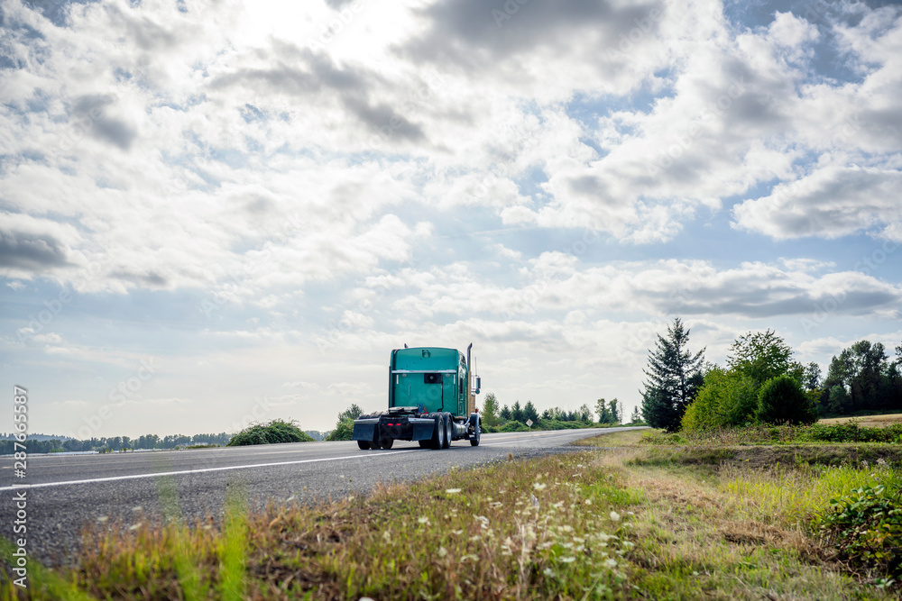 Big rig green classic semi truck tractor running to warehouse for picking up loaded semi trailer for next delivery Big rig green classic semi truck tractor running to warehouse for picking up loaded semi trailer for next delivery