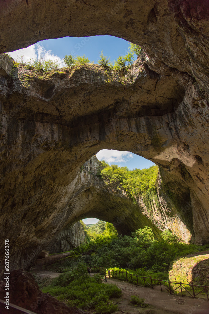 Odd beautiful cave with green plants inside and wholes in the ceiling with blue skies