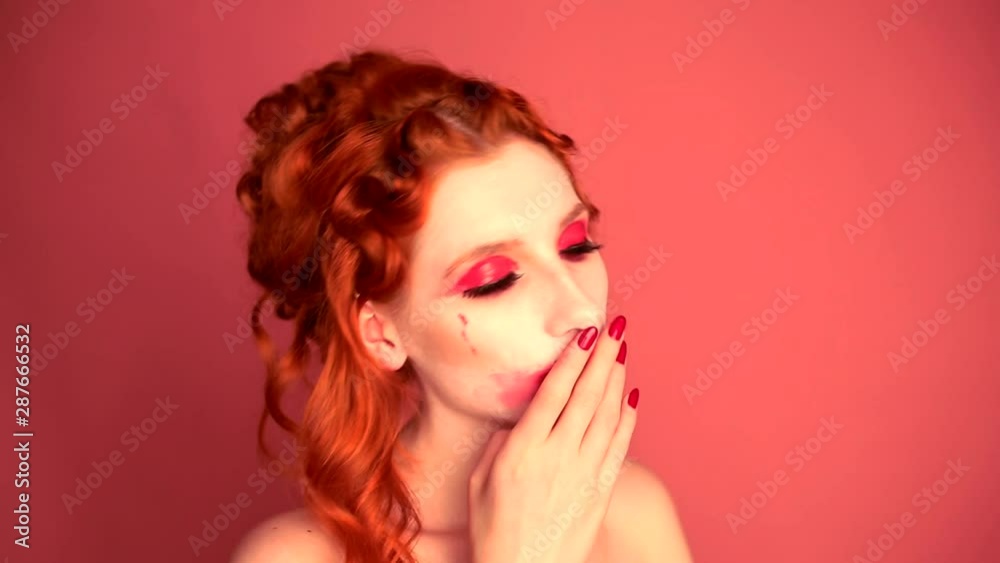 Girl with red hair with a frightening make-up on a pink background. Halloween look with pale skin. Redhead woman wash off makeup on face. Scary vampire in the studio. Manicure on hands. Red nails Girl with red hair with a frightening make-up on a pink background. Halloween look with pale skin. Redhead woman wash off makeup on face. Scary vampire in the studio. Manicure on hands. Red nails