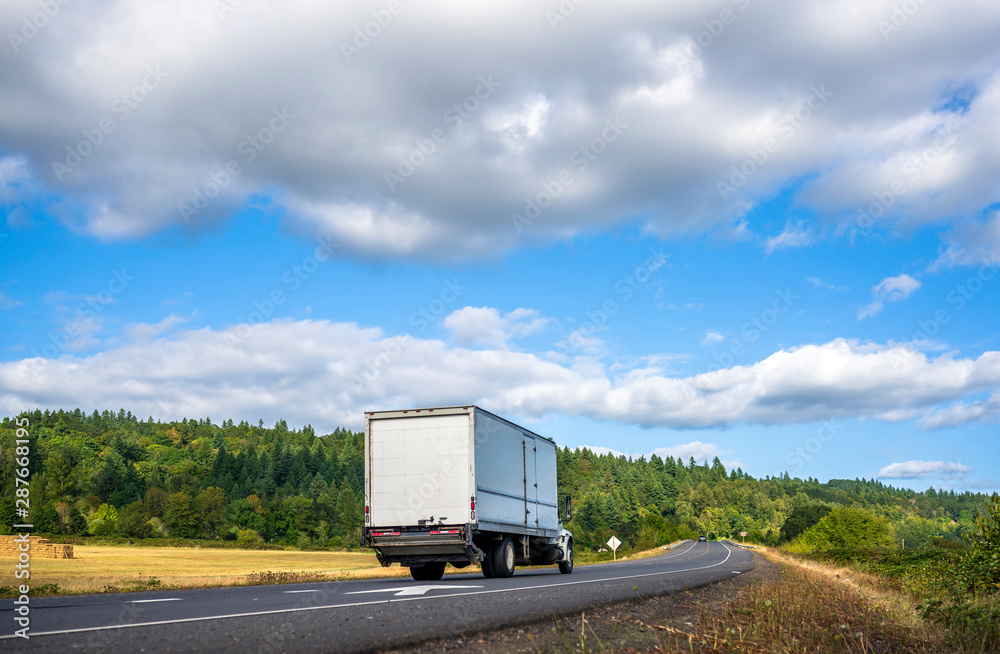 Compact big rig semi truck with long box trailer running on the road for delivery commercial goods Compact big rig semi truck with long box trailer running on the road for delivery commercial goods
