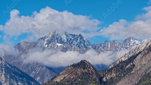 Amazing rock mountain peak among white clouds with blue sky background in Tibet plateau, China.