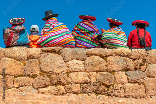 A group of Quechua indigenous women in traditional clothing and a young boy sitting and chatting on an ancient Inca wall in the archaeological site of Chinchero in the region of Cusco city, Peru. photo
