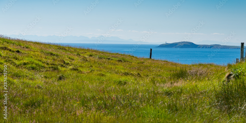 Panorama view from top of cliff in Outer Hebrides, Scotland showing lighthouse and far distant mountains