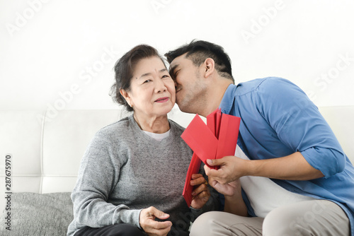 Happy Asian mother give red envelopes containing cash to her son for Chinese New Year concept.