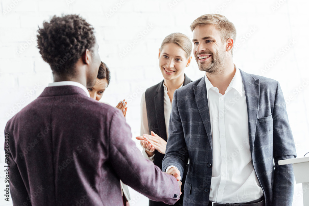 four multiethnic colleagues in formal wear talking and shaking hands four multiethnic colleagues in formal wear talking and shaking hands