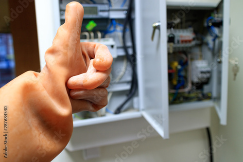 an open electric box with electro-automatics and a hand in a dielectric silicone glove with a raised thumb up