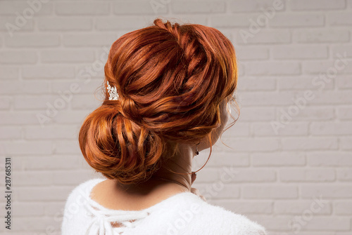 Female hairstyle low bun on the head of a red-haired model back view.