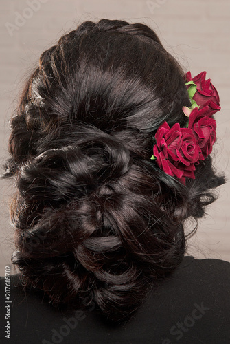 Female hairstyle low bun with rosebuds on the head of a brunette back view.