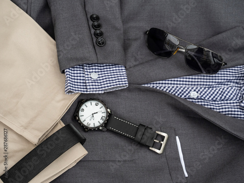 Creative fashion design for men casual clothing set and accessories on wooden background include gray suit, pants, belt, sunglasses, watch and scottis office shirt. Flat lay, top view
