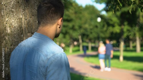 Man secretly spying loving couple walking on date outdoors, jealous ex-boyfriend photo