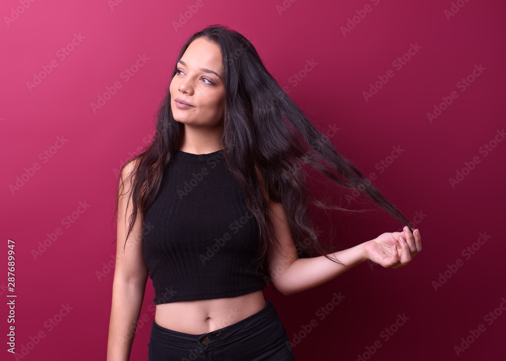 pretty brunette girl in front of a red background stretches her hair carelessly while looking away pretty brunette girl in front of a red background stretches her hair carelessly while looking away