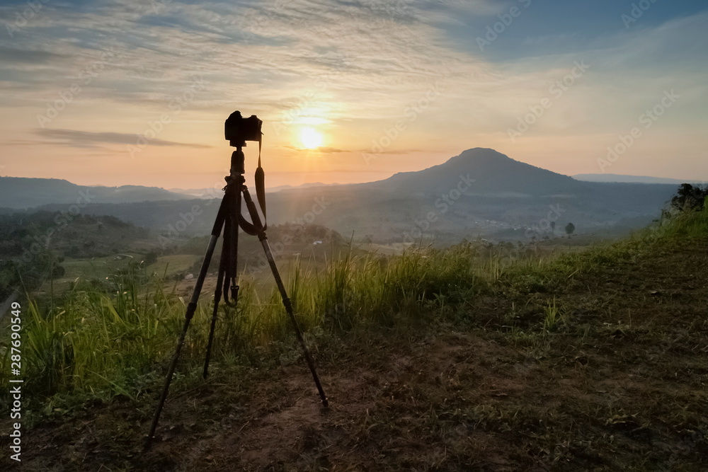 Mountain view silhouette a camera on tripod with yellow sun light and cloudy sky background, sunrise at Khao Takhian (Takian) Ngo, Khao Kho, Phetchabun, Thailand.