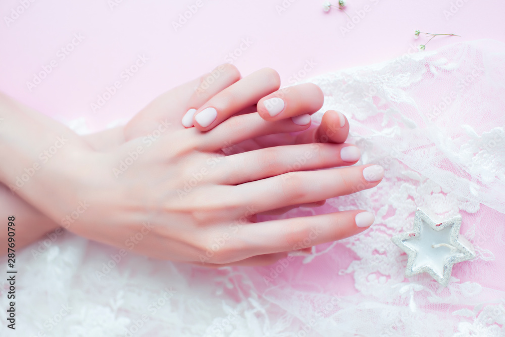 Fototapeta premium woman hands with manicure among white lace on pink background, cosmetic concept