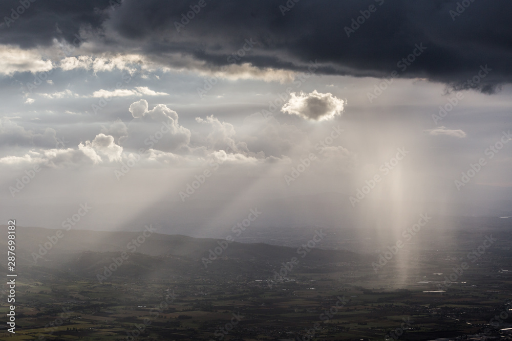 Sunray shines through clouds and rain over the mountains in the middle of shadows