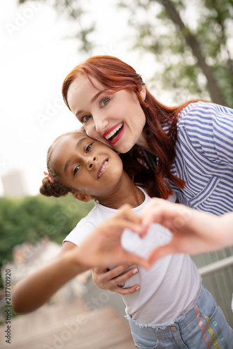 Red-haired woman with bright lips hugging her funny daughter