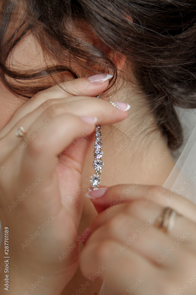 Wedding day. Wedding earrings on a female hand, she takes the earrings, the bride fees, morning bride, white dress, wear earrings. Earrings close-up in the hands of the bride. jewelry accessories