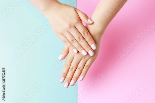 Female hands with white manicure on a pink and blue background  top view