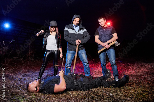 Three bandits near dead man in the field at night. Photoshoot about life of gungsters in Russia photo