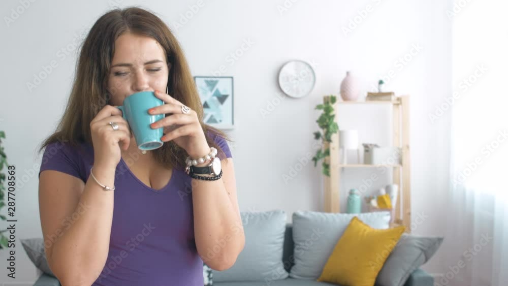 Portrait of young girl standing in living room with blue cup of coffee or tea. Close up of woman at home. 4k slow motion footage. Portrait of young girl standing in living room with blue cup of coffee or tea. Close up of woman at home. 4k slow motion footage.