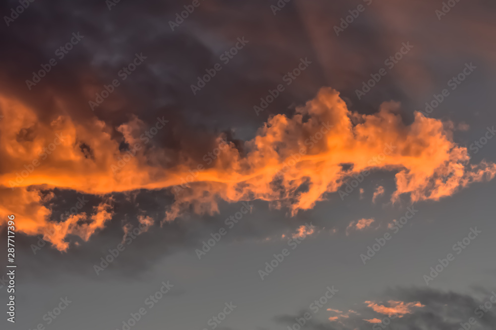 Fototapeta premium Dark cloud reflecting orange glow at sunset.