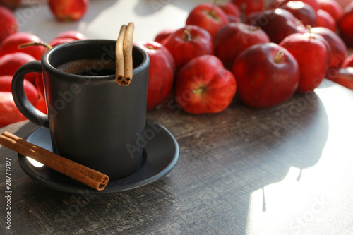 Red apples, cup of coffee and cinnamon sticks on grey wooden boards or desk. Closeup. Autumn, fall, morning, breakfast, healthy food concept