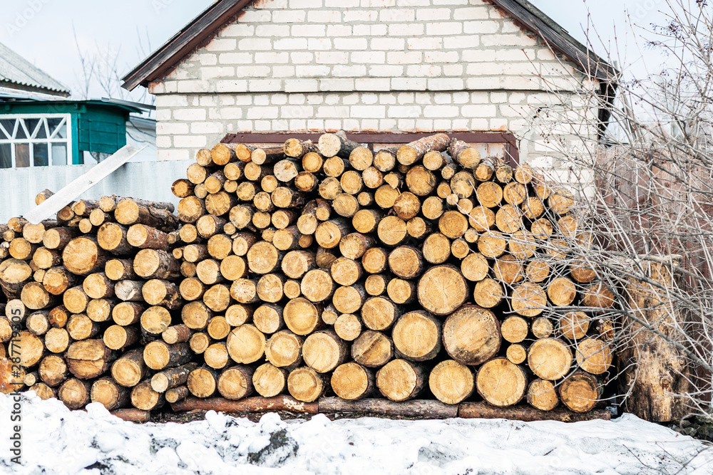 Firewood log rows stacked near old country white brick house wall. Logging and preparation for geating in winter and cold season Firewood log rows stacked near old country white brick house wall. Logging and preparation for geating in winter and cold season