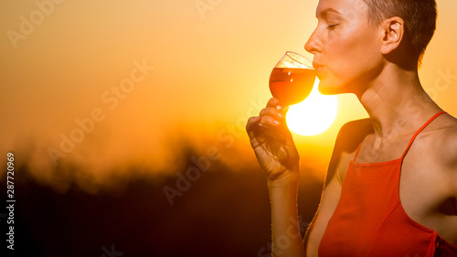 Happy brunette woman holding orange cocktail over sunset sky in orange colors