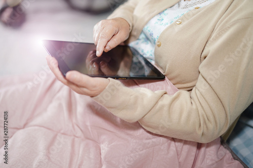 Asian senior or elderly old lady woman patient holding in her hands digital tablet and reading emails while sitting on bed in nursing hospital ward : healthy strong medical concept 