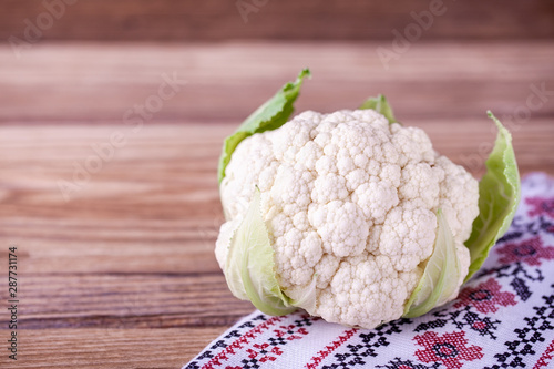 Raw cauliflower on wooden background with patterned napkin. Free copy space