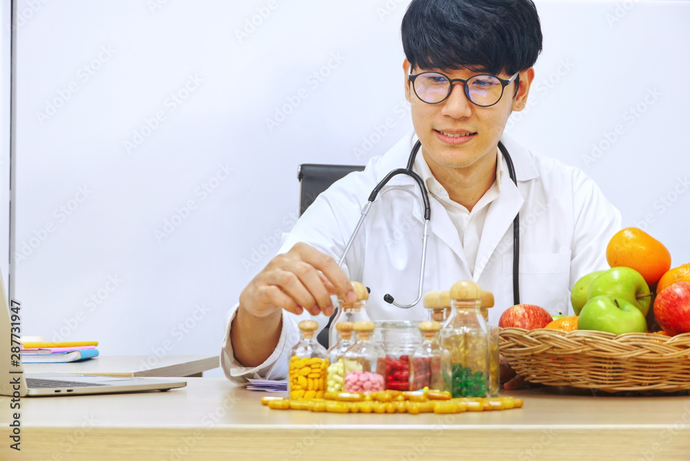Asia nutritionist pick up supplyment bottle on working table which have group of fruits in the basket Asia nutritionist pick up supplyment bottle on working table which have group of fruits in the basket