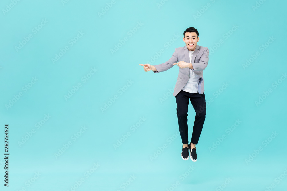 Young smiling Asian man jumping and pointing hands to copy space