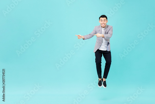 Young smiling Asian man jumping and pointing hands to copy space