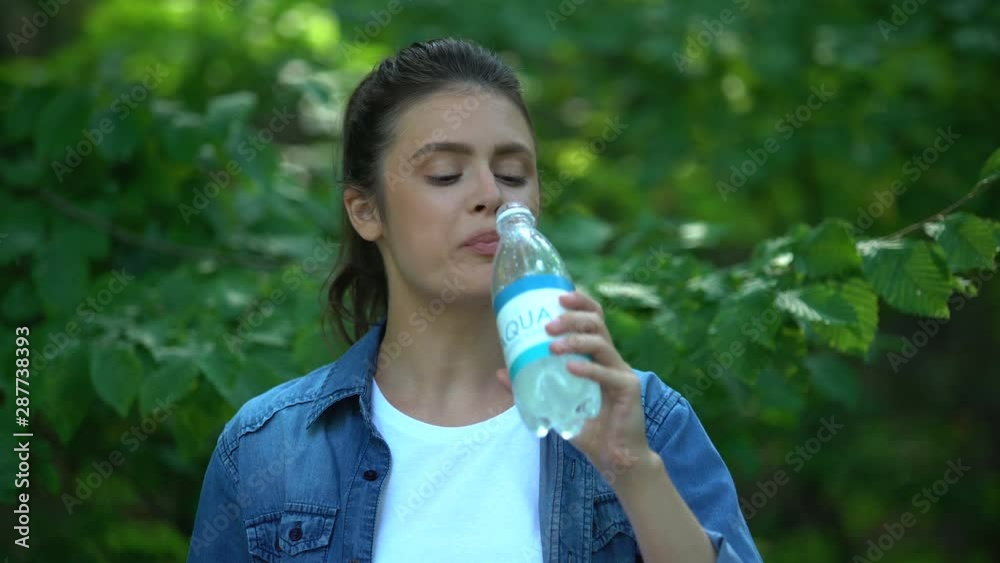 Young woman drinking mineral water enjoying rest in green forest, fresh air Young woman drinking mineral water enjoying rest in green forest, fresh air