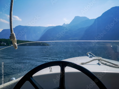 Boat in the middle of the lake with view in the foreground of the steering wheel and deep water in the background with the sun's rays entering between the great mountains of the Alps