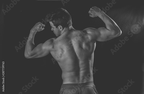 Young fitness muscly man showing his back,shoulders, triceps and biceps muscles after training