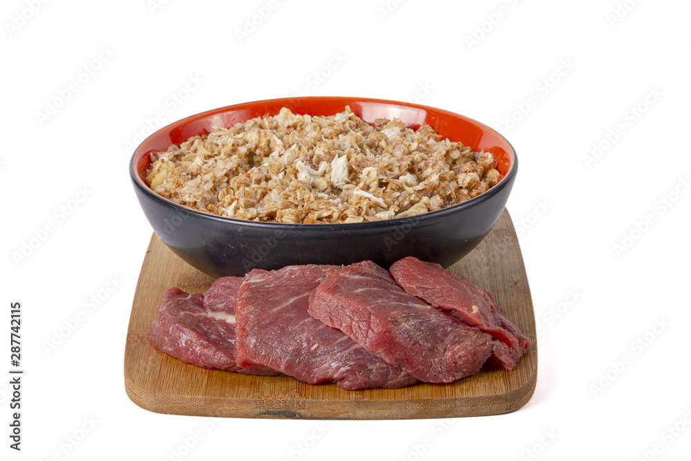 Sprouted wheat porridge in red and black bowl with raw beef meat near it. On wooden desk. Isolated on white background. Idea for healthy diet meal. Sprouted wheat porridge in red and black bowl with raw beef meat near it. On wooden desk. Isolated on white background. Idea for healthy diet meal.